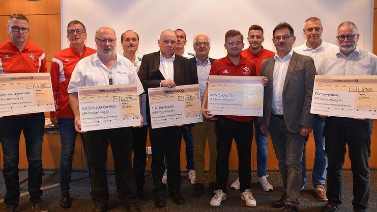 Gruppennahaufnahme von Männern mit Schecks für DFB-Bonuszahlungen, hinter ihnen ein heller Hintergrund und eine neutralen Umgebung.