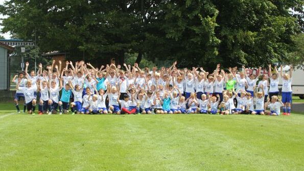 Gruppenfoto von über 70 Kindern in Sportbekleidung, die auf einer Wiese stehen und die Arme jubelnd heben.