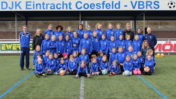 Gruppenfoto der Fußballmannschaft DJK Eintracht Coesfeld mit Jugendlichen in blauen Trikots auf einem Kunstrasenplatz.