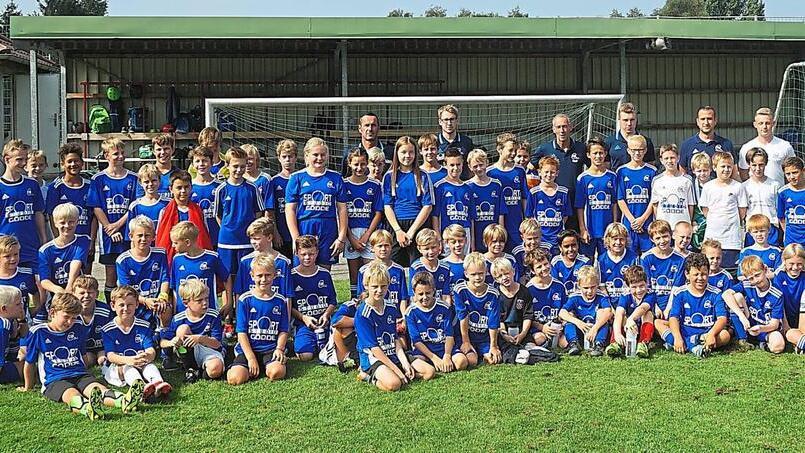 Gruppenfoto einer Fußballmannschaft mit Kindern und Trainern in blauen Trikots auf einem Sportplatz.