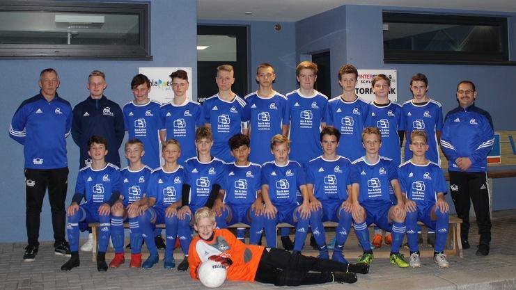 Mannschaftsfoto einer Jugendfußballmannschaft in blauen Trikots, posaunen um einen Trainer. Im Vordergrund ein lesender Torwart.