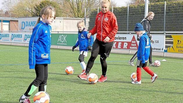 Übungseinheit auf einem Fußballplatz mit Kindern, die mit einem Trainer an ihren Dribbling-Fähigkeiten arbeiten.