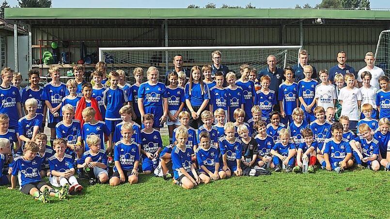 Gruppenfoto einer Fußballmannschaft mit Kindern und Trainern in blauen Trikots auf einem Sportplatz.