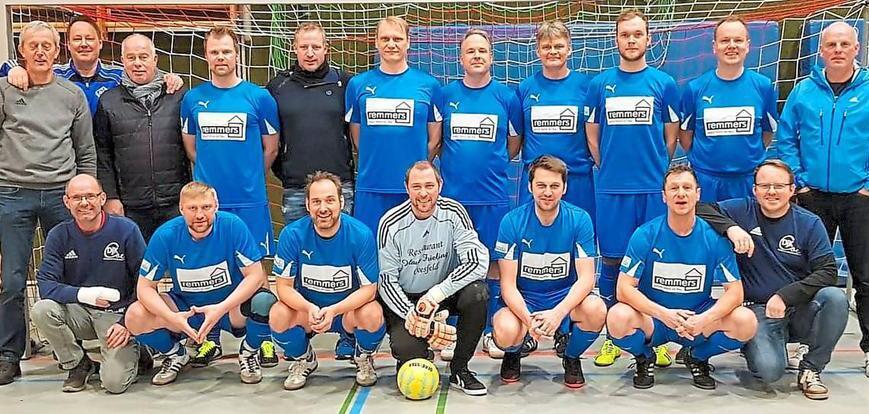 Gruppenfoto einer Fußballmannschaft in blauen Trikots, aufgestellt vor einem Tor in einer Sporthalle.