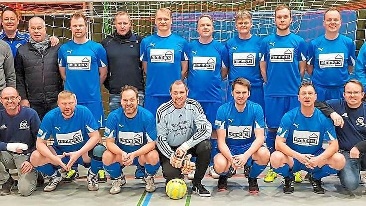 Gruppenfoto einer Fu&szlig;ballmannschaft in blauen Trikots, aufgestellt vor einem Tor in einer Sporthalle.