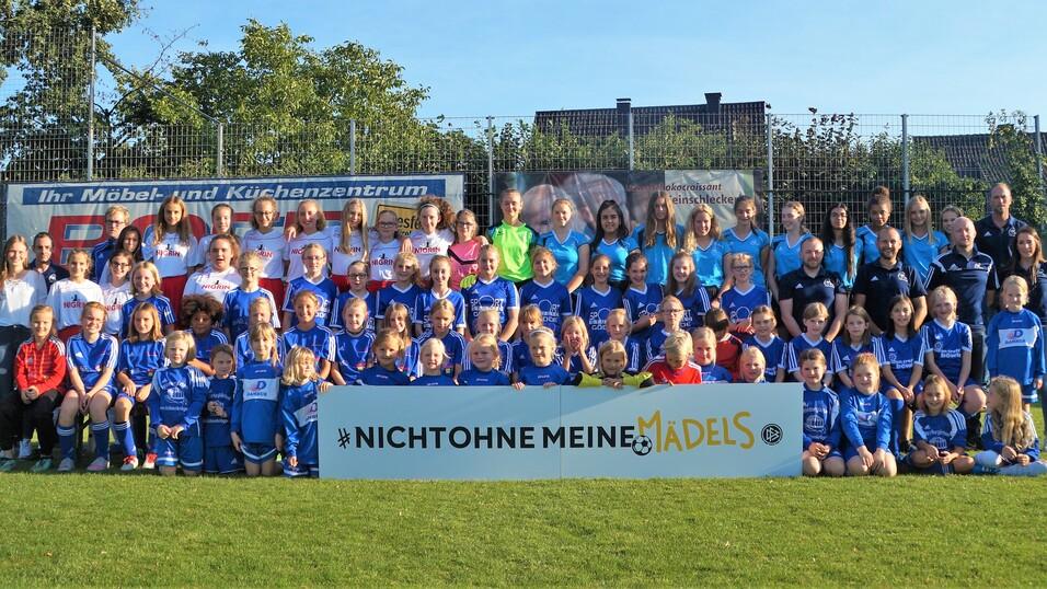 Gruppenfoto von Mädchen- und Frauenfußballspielern in blauen Trikots, posierend vor einem Banner mit dem Slogan „#NICHTOHNE MEINE MÄDELS“.