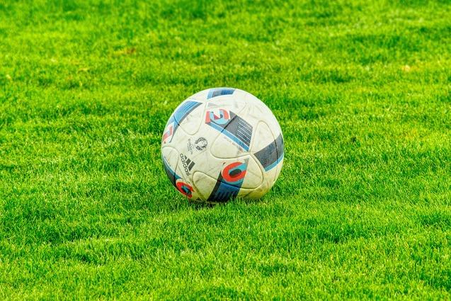 Fußball mit blauen und roten Akzenten auf intensiv grünem Rasen.