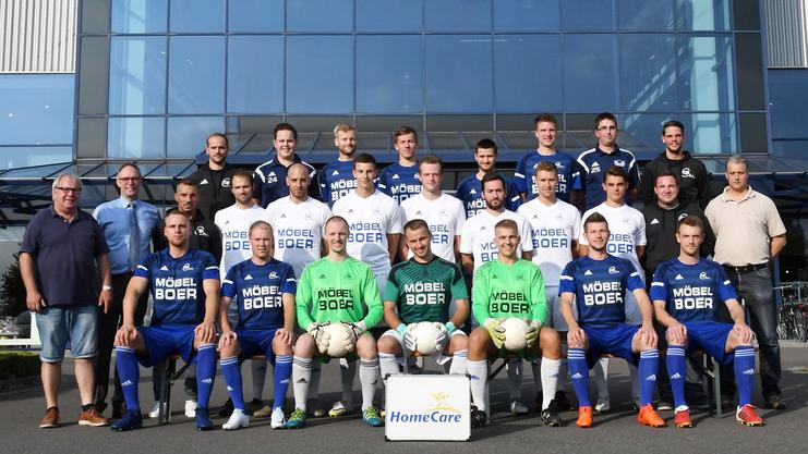 Gruppenfoto einer Fußballmannschaft vor einem Gebäude mit dem Schriftzug "BOER", Spieler in blauen und weißen Trikots.