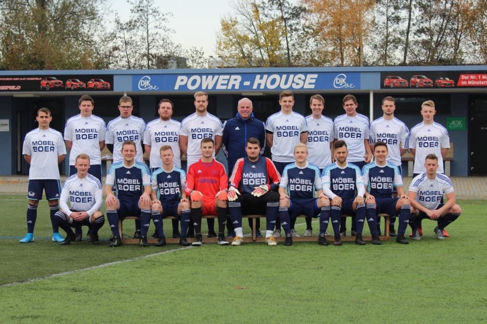 Mannschaftsfoto einer Fußballmannschaft mit Spielern in weißen und blauen Trikots auf einem Sportplatz.