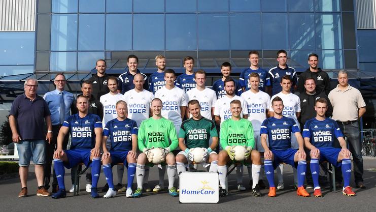 Gruppenfoto einer Fußballmannschaft vor einem Gebäude mit dem Schriftzug "BOER", Spieler in blauen und weißen Trikots.