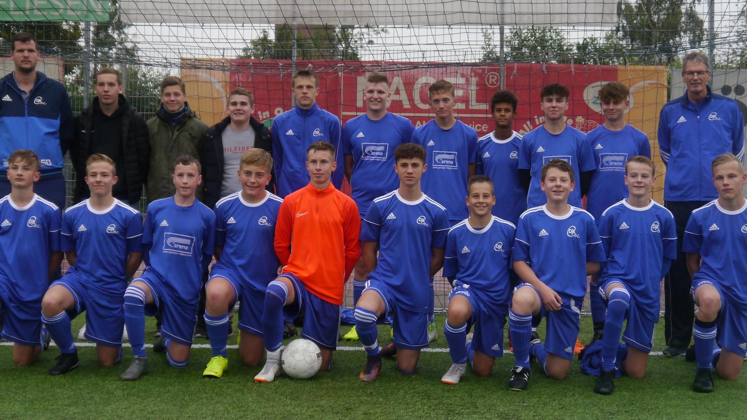 Gruppenbild einer Jugendfußballmannschaft in blauen Trikots, auf einem Platz neben dem Tor stehend, mit Trainern.