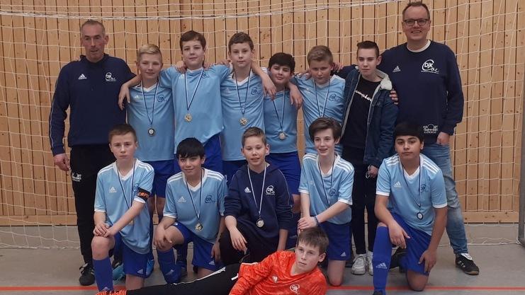 Mannschaftsfoto einer Jugendfußballmannschaft in blauen Trikots mit Medaillen, gestanden vor einem Fußballnetz.