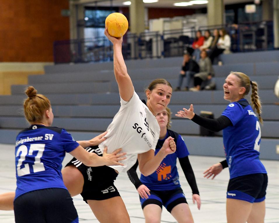 Spielszene im Handball: Spielerin in Weiß wirft Ball, während gegnerische Spielerinnen in Blau versuchen, sie zu blockieren.