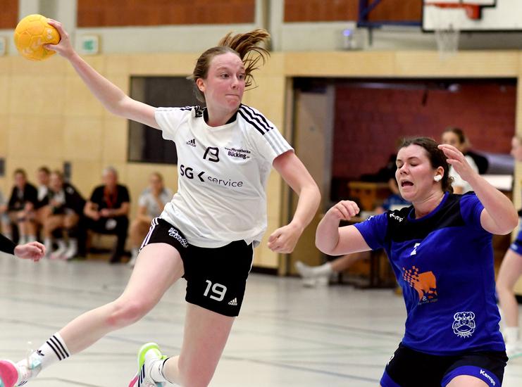 Sprung einer Handballspielerin in einem weißen Trikot, während eine Gegenspielerin in blau versucht zu blocken.
