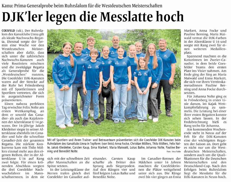 Gruppe von Kajakfahrern in blauen T-Shirts, stehen lächelnd am Ufer eines Flusses, mit Trainer im Hintergrund.