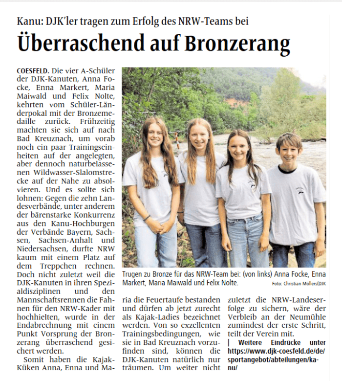 Vier Schüler der DJK-Kanuten stehen lächelnd am Ufer eines Gewässers, im Hintergrund grüne Bäume und Felsen.
