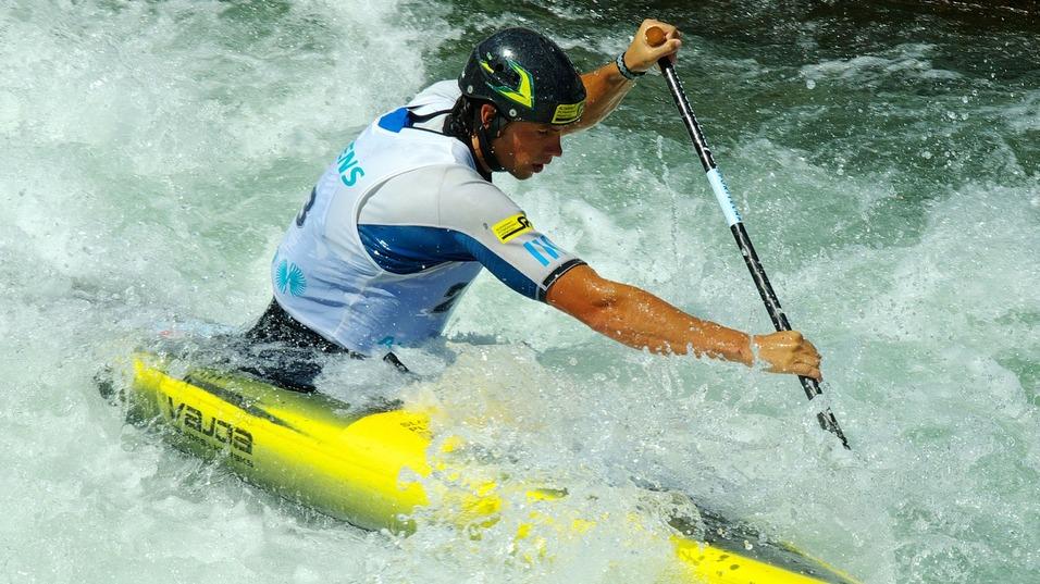 Kajakfahrer paddelt durch schäumende Wellen in einem Wildwasserkanal. Gelbes Kajak ist deutlich sichtbar.