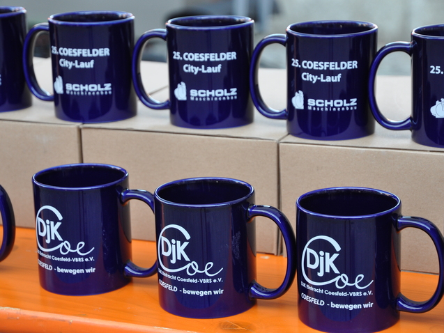 Mehrere blaue Tassen mit Aufdrucken zum 25. Coesfelder City-Lauf stehen auf einem Tisch.