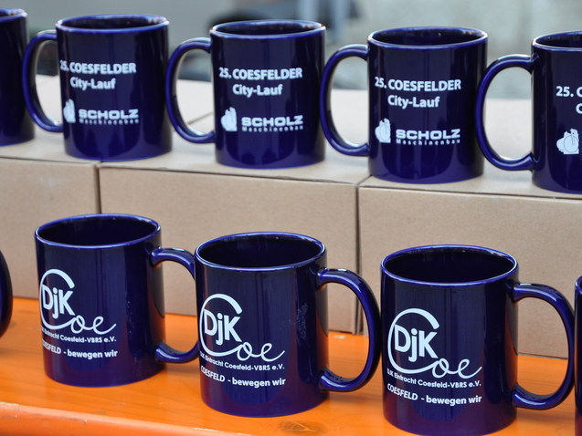 Mehrere blaue Tassen mit Aufdrucken zum 25. Coesfelder City-Lauf stehen auf einem Tisch.