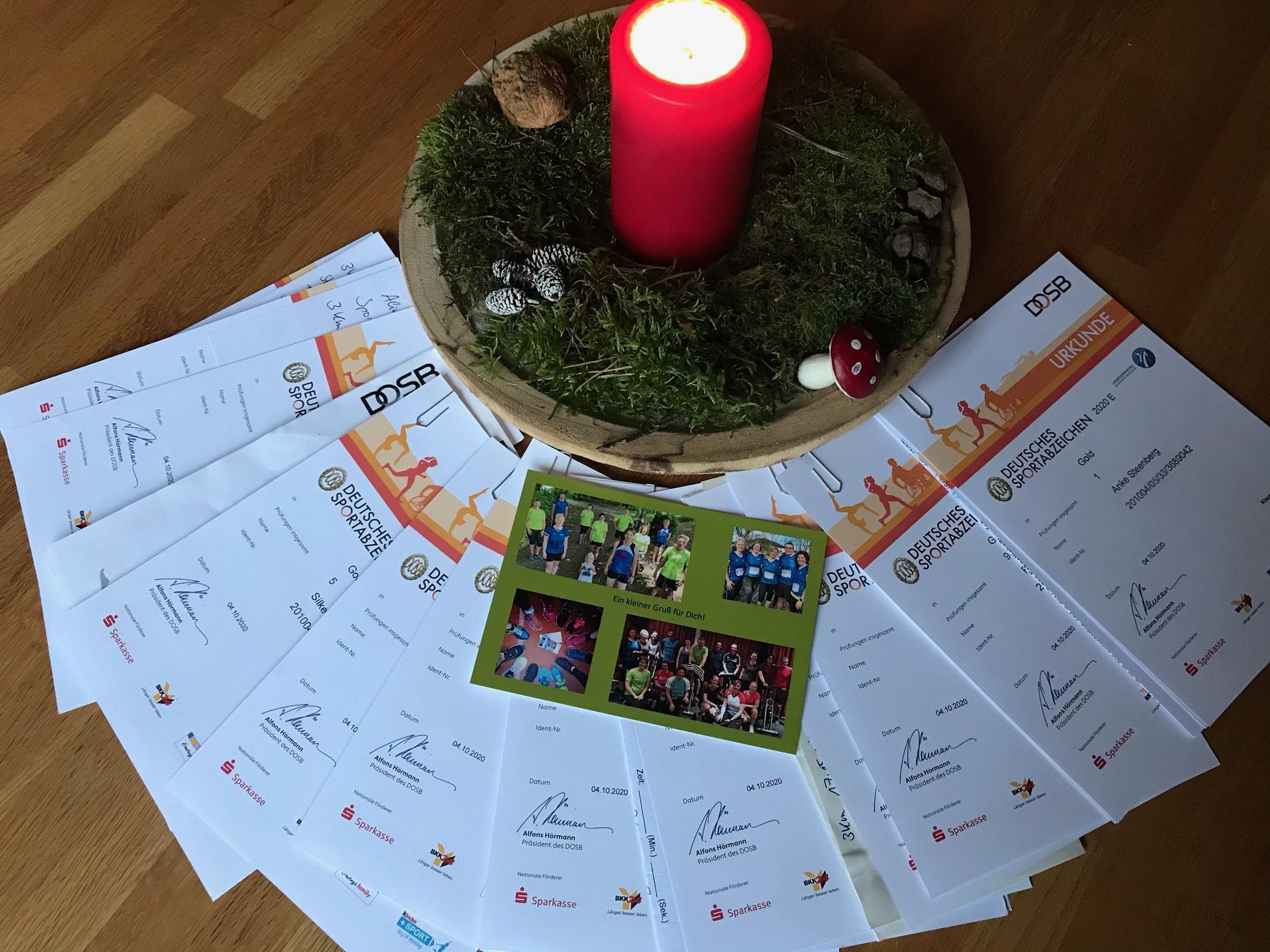 Sammlung von Urkunden des Deutschen Olympischen Sportbundes auf einem Tisch, umgeben von einem Adventsgesteck.