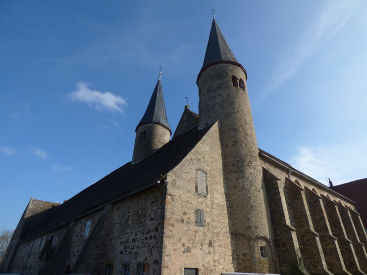 Ansicht einer steinernen Kirche mit zwei spitzen Türmen unter blauem Himmel.