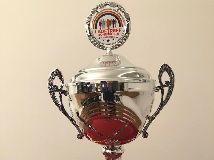 Silberner Pokal mit Aufschrift &bdquo;Sieger 2021&ldquo; und buntem Logo auf rotem Untergrund.