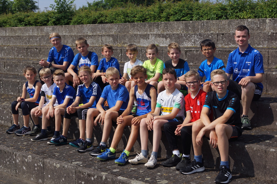 Gruppe von Kindern in Sportbekleidung, sitzend auf einer Steinbank, lächeln in die Kamera.