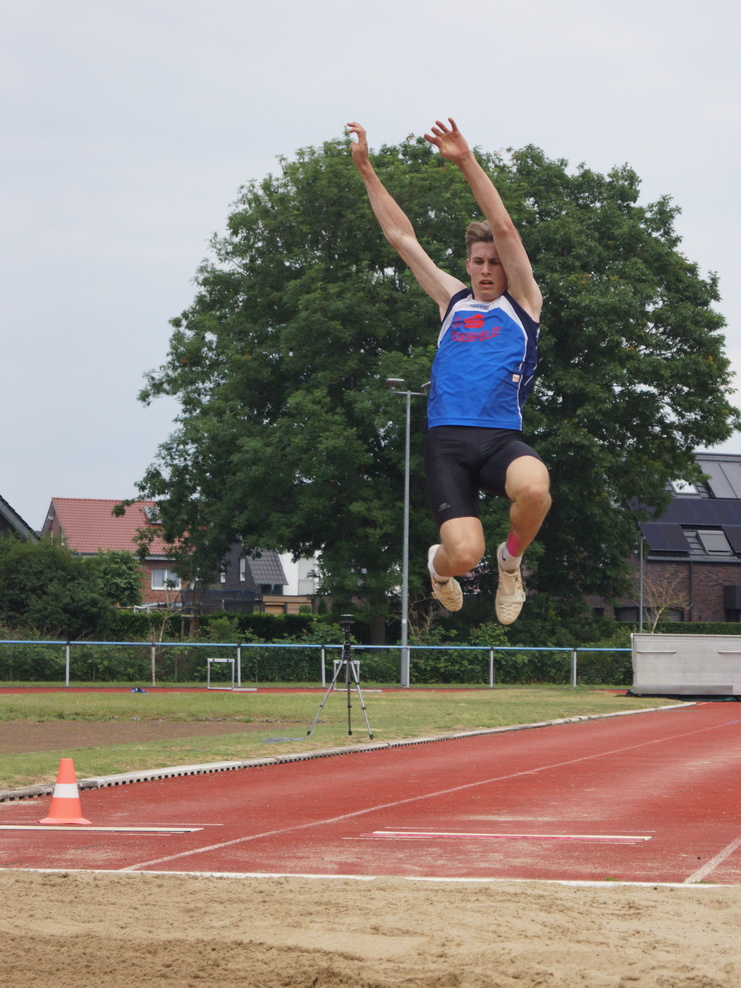 Aktiver Athlet beim Weitsprung, der mit gestreckten Beinen in der Luft über einen Sandgrubenrand springt.