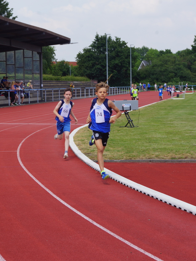 Zwei Jungen in blauen Lauftrikots laufen auf einer roten Laufbahn bei einem Wettkampf.