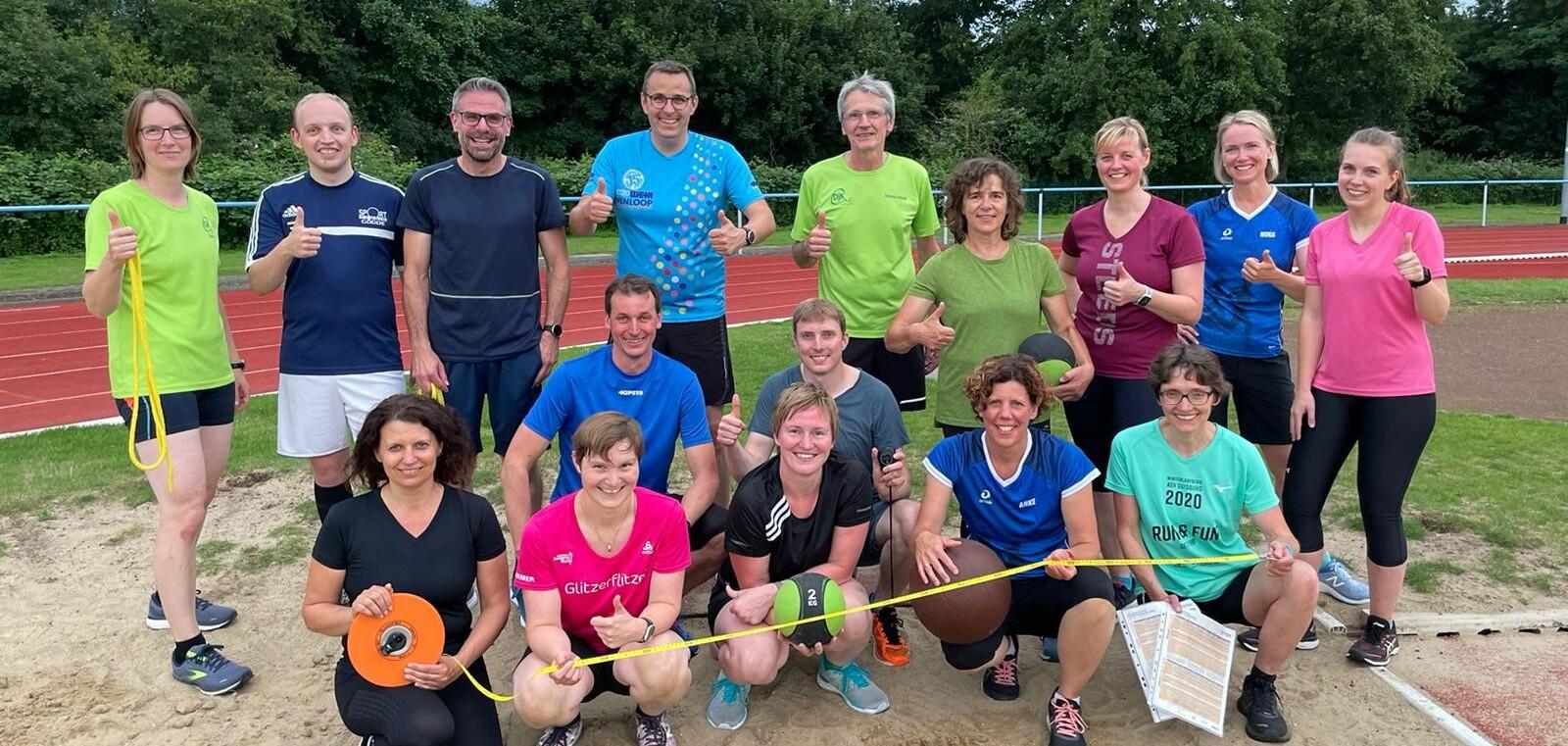 Gruppe von Sportlern auf einer Laufbahn im Freien, lobend mit Daumen hoch, umgeben von Trainingsgeräten und -materialien.