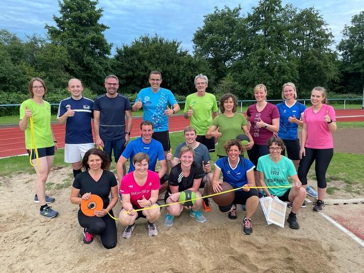 Gruppe von Sportlern auf einer Laufbahn im Freien, lobend mit Daumen hoch, umgeben von Trainingsgeräten und -materialien.