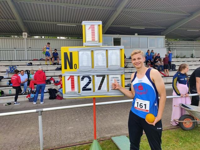 Athlet mit orangefarbenem Ball steht neben einem Punkte-Display mit der Zahl 127 auf einem Sportplatz.
