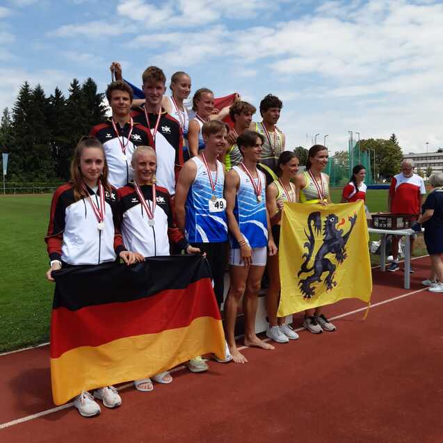 Gruppenszene von Athleten mit Medaillen, die stolz Fahnen von Deutschland und Flandern auf einem Sportplatz halten.