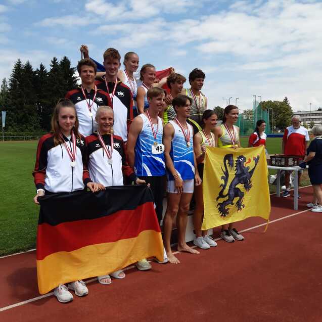 Gruppenszene von Athleten mit Medaillen, die stolz Fahnen von Deutschland und Flandern auf einem Sportplatz halten.