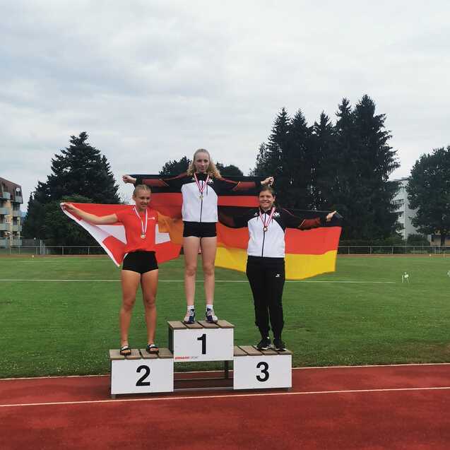 Drei Athletinnen auf dem Siegertreppchen: Erste mit Medaille, deutsche und schweizerische Flagge als Hintergrund.