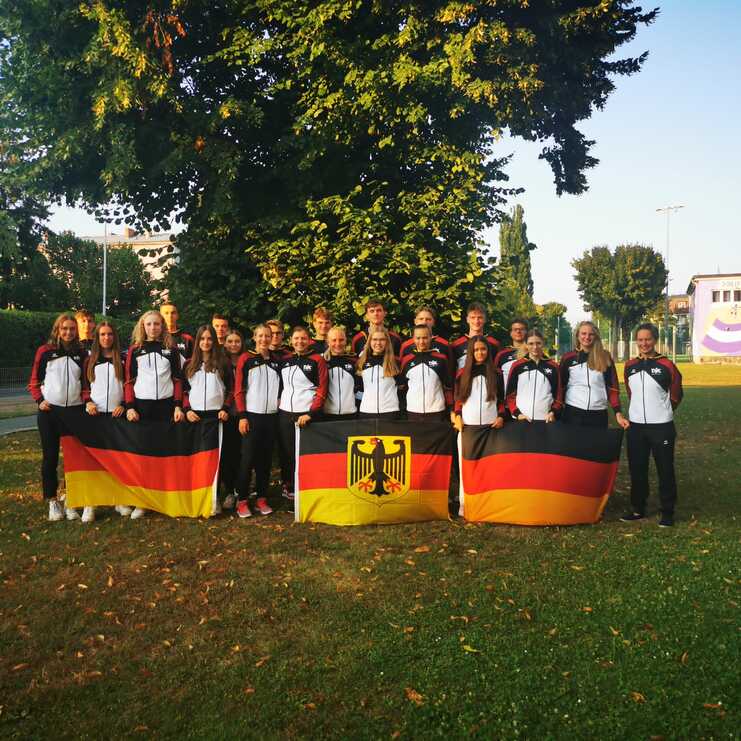 Gruppe junger Sportler in Jacken mit deutschen Farben, posiert im Freien mit der deutschen Flagge.