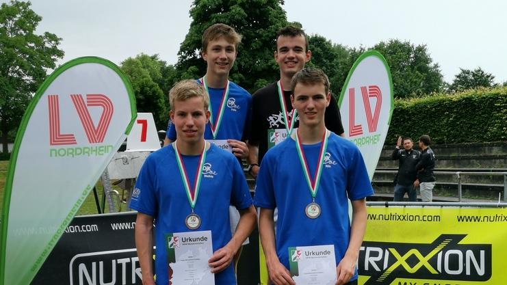 Vier Jugendliche stehen auf dem Siegertreppchen, tragen Medaillen und halten Urkunden in den Händen.