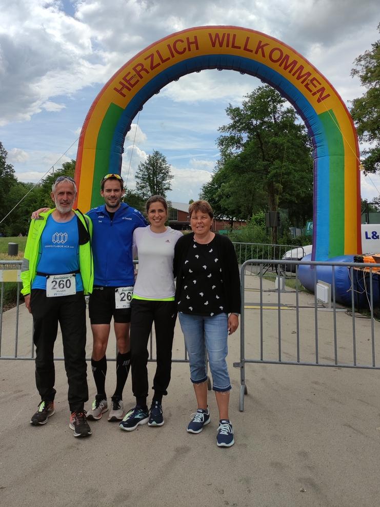 Vier Personen posieren vor einem bunten, aufblasbaren Willkommensbogen bei einer sportlichen Veranstaltung im Freien.