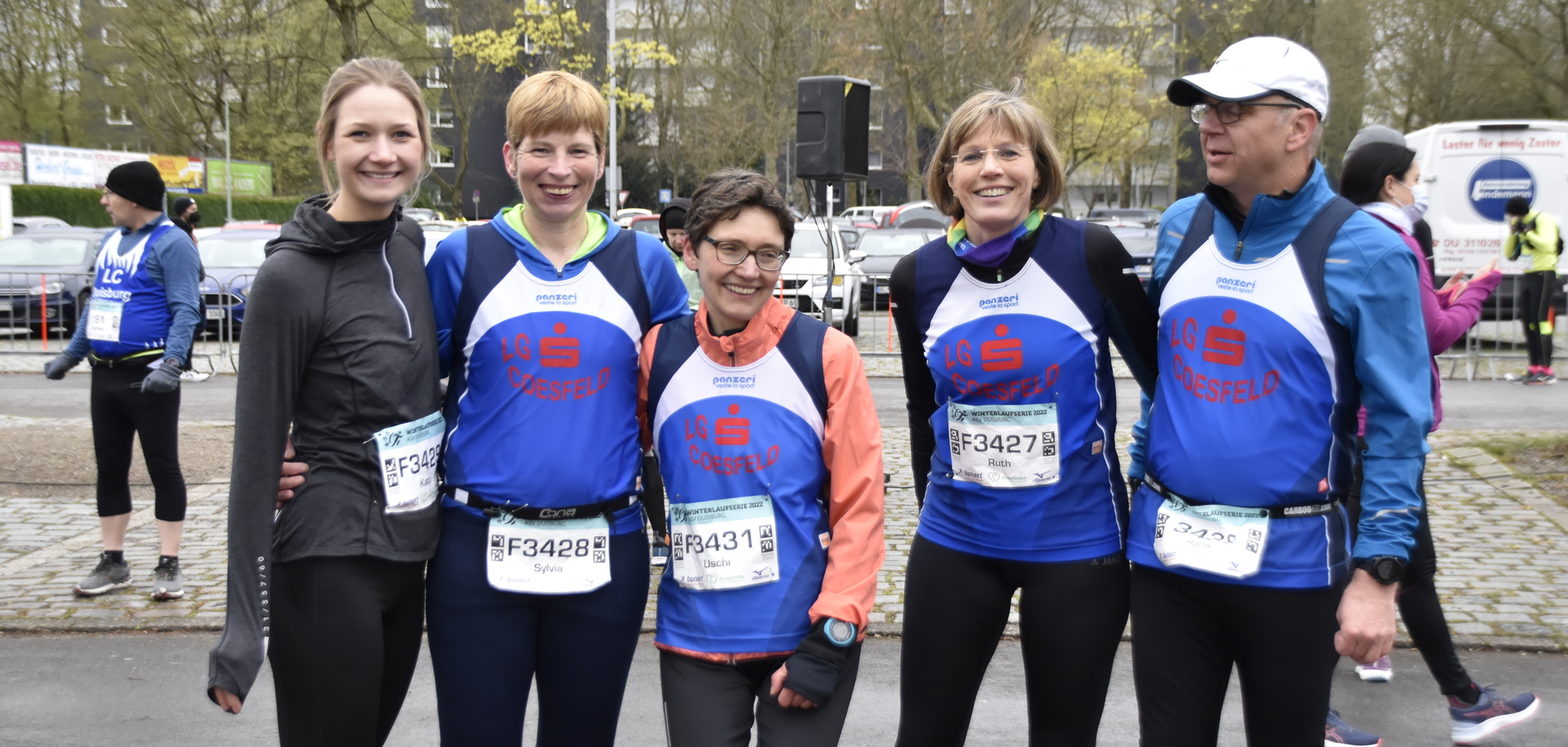 Fünf Läufer in Teamkleidung stehen lachend zusammen, bereit für einen Wettkampf in einem urbanen Umfeld.