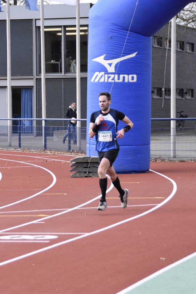 Mann l&auml;uft auf einer Laufbahn, im Hintergrund sind Zuschauer und ein gro&szlig;er Startbogen sichtbar.