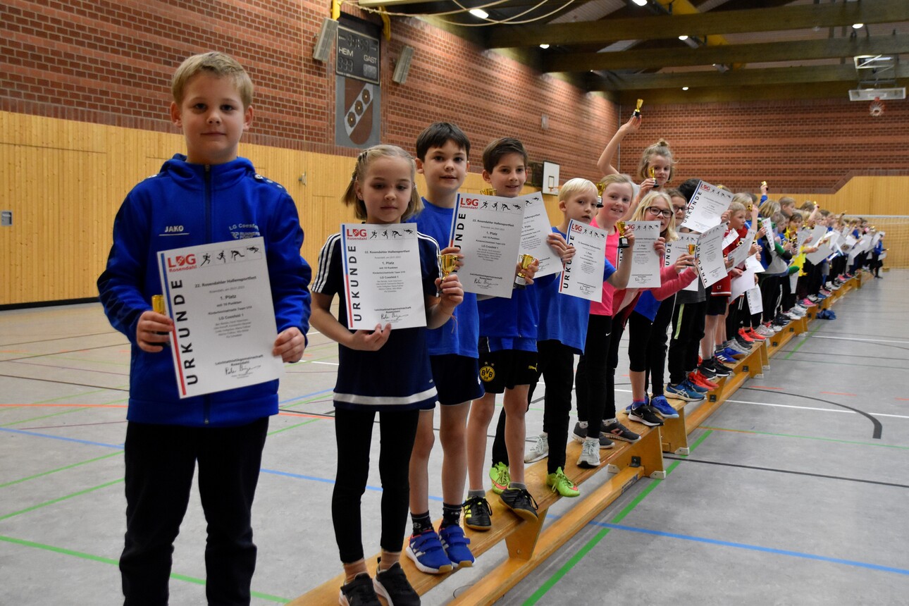 Mehrere Kinder stehen in einer Sporthalle nebeneinander und halten Urkunden nach einem Wettkampf in den Händen.
