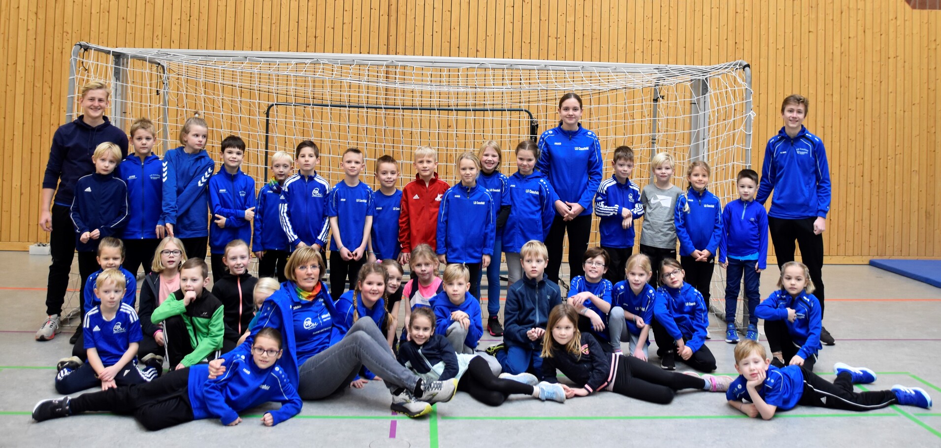 Gruppe von Kindern und Trainern in blauen Sportanzügen vor einem Toreinsatz in einer Sporthalle.