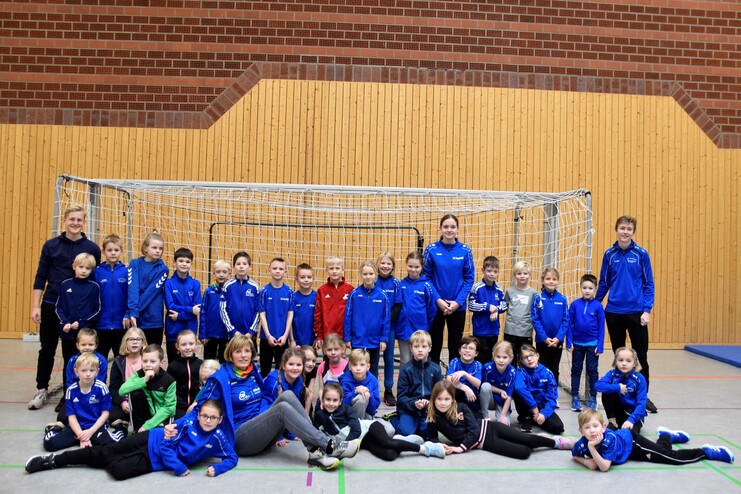 Gruppe von Kindern und Trainern in blauen Sportanzügen vor einem Toreinsatz in einer Sporthalle.