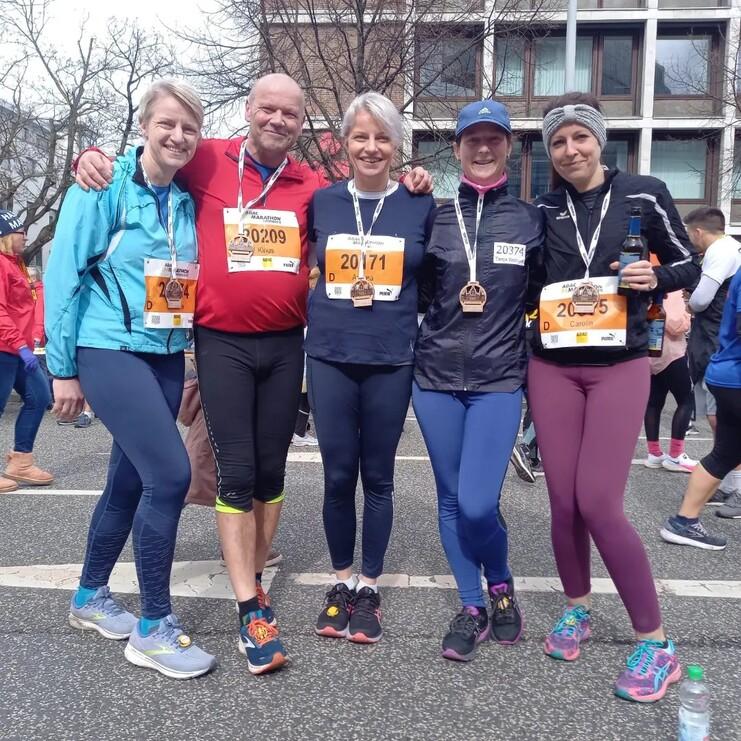 Fünf Läufer in Sportkleidung stehen nach einem Rennen zusammen, Medaillen und Startnummern sichtbar.