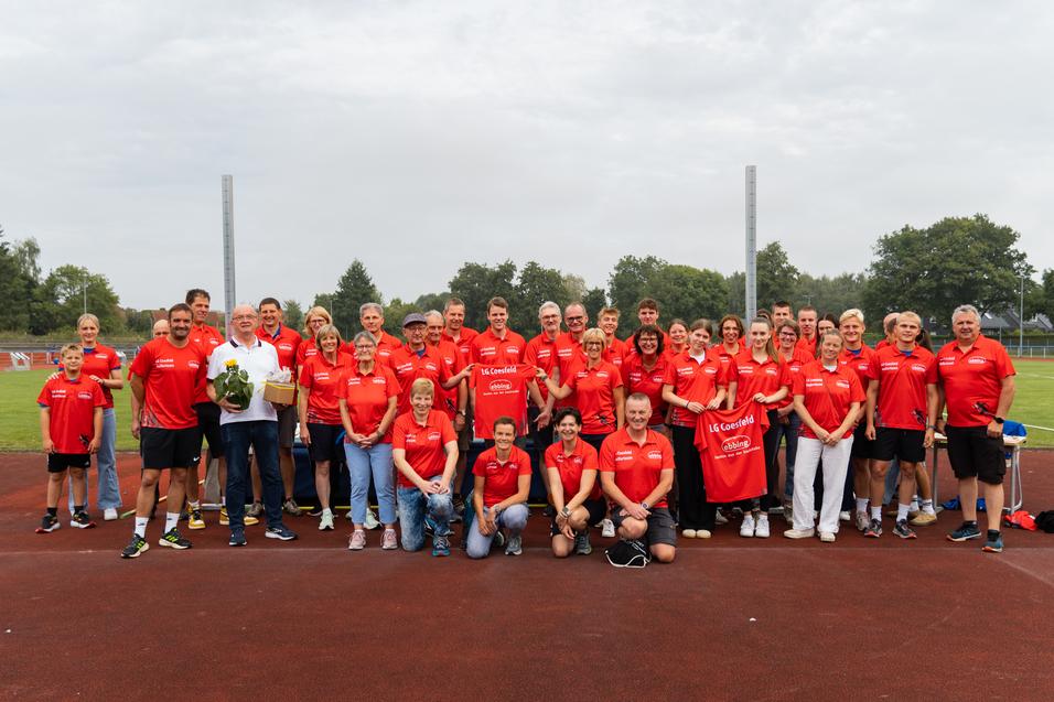 Gruppenfoto von Sportlern in roten T-Shirts, versammelt auf einem Leichtathletikplatz, mit Blumen und Geschenken.