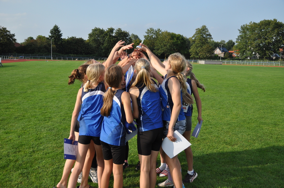 Eine Gruppe von Mädchen in blauen Sporttrikots jubelt gemeinsam auf einem grünen Rasenfeld.