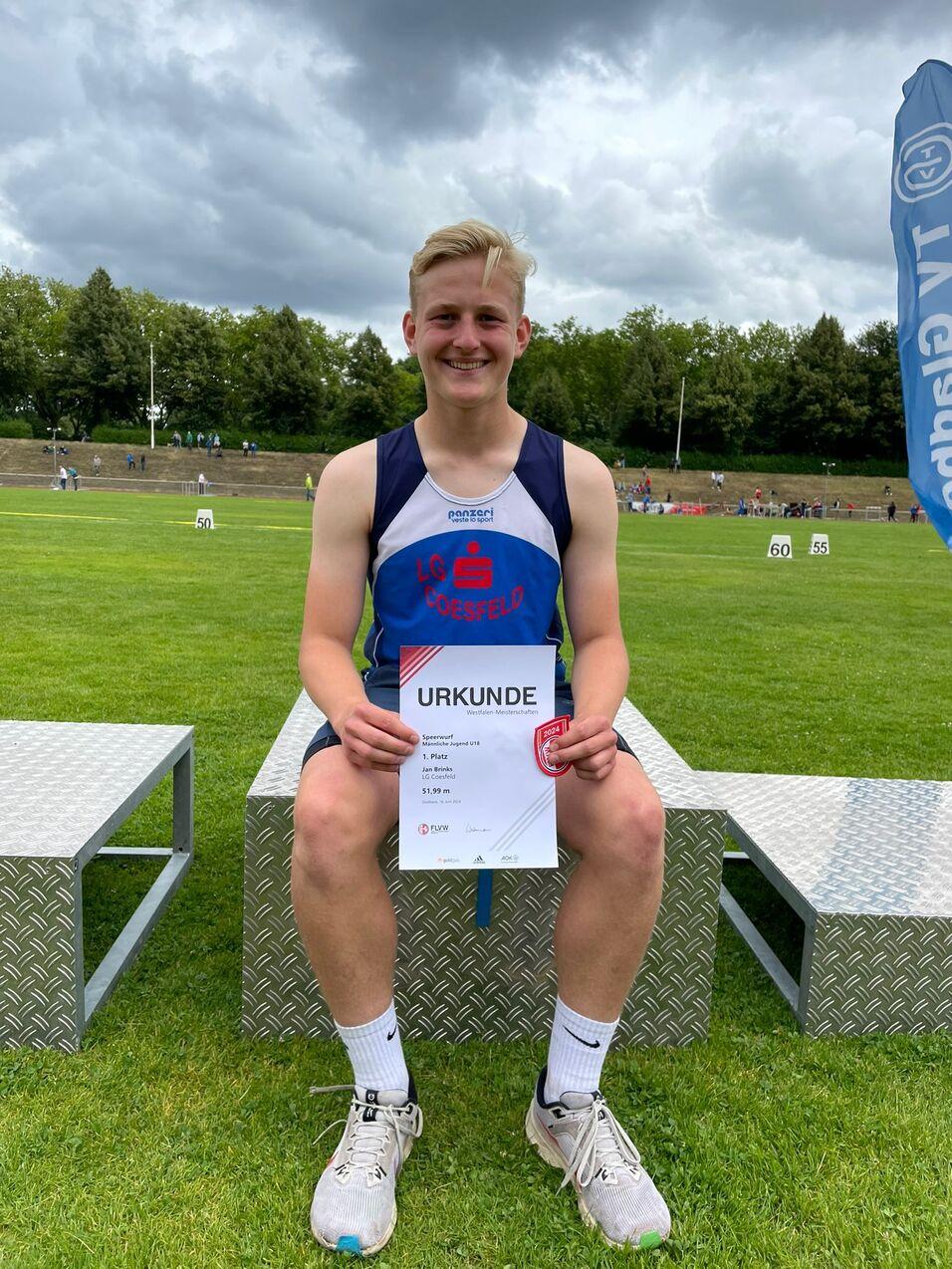 Junger Athlet sitzt auf einer Bank und hält stolz seine Urkunde für den ersten Platz im Speerwurf in der Hand.
