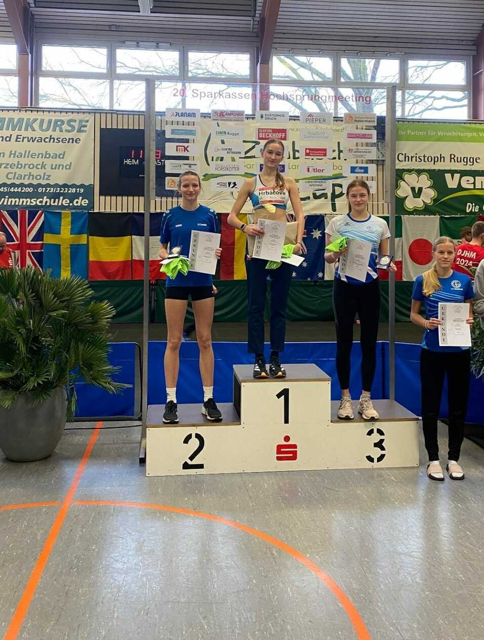 Vier Athletinnen stehen auf dem Siegertreppchen mit Urkunden beim 20. Sparkassen Hochsprungmeeting in einer Sporthalle.
