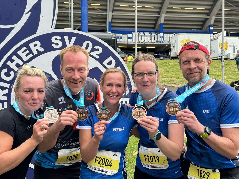 Fünf Läufer/innen mit Medaillen in der Hand nach erfolgreichem Marathon