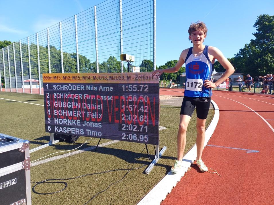 Junger Athlet mit Startnummer 1172 steht neben einer Anzeigetafel mit Ergebnissen eines 800m-Laufs auf der Leichtathletikbahn.